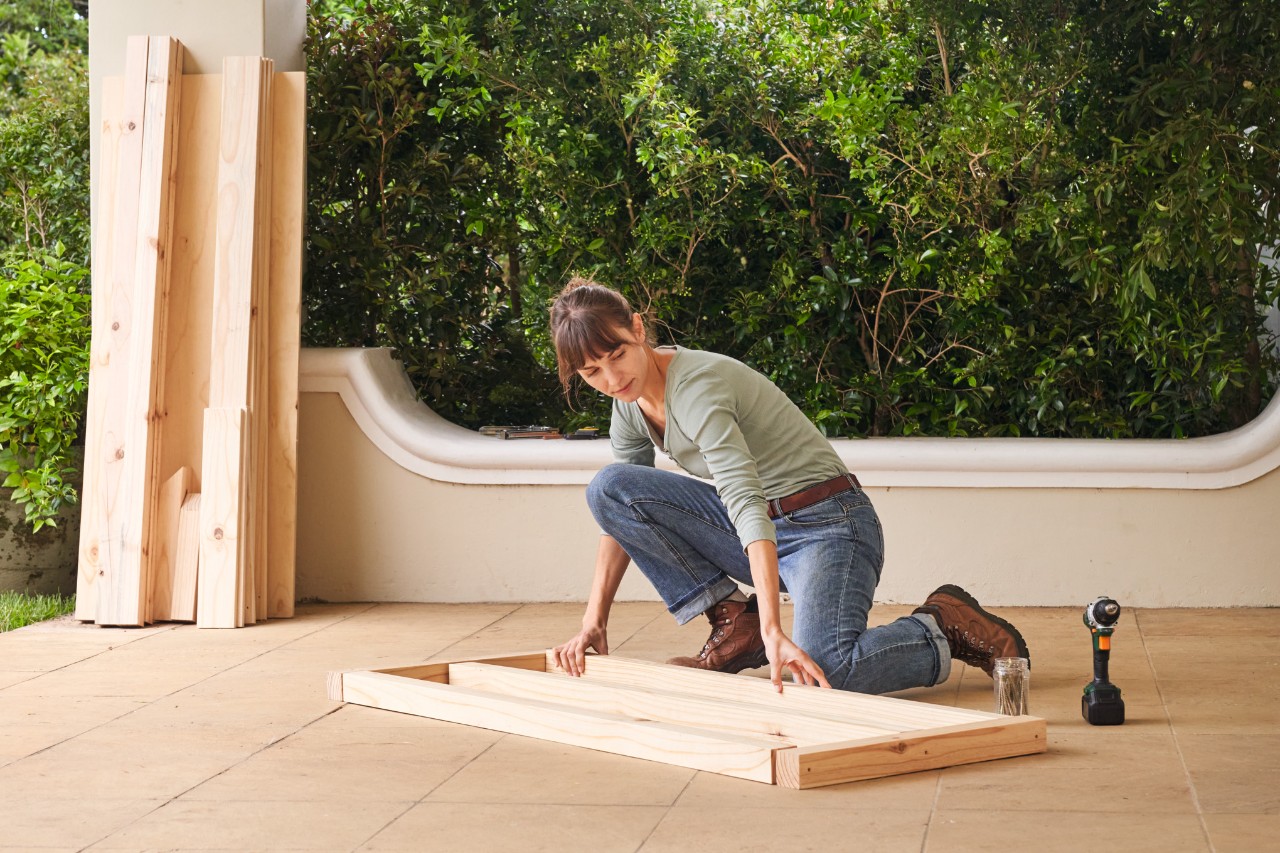 Een vrouw plaatst de houten onderdelen voor de onderste dakconstructie op een terras