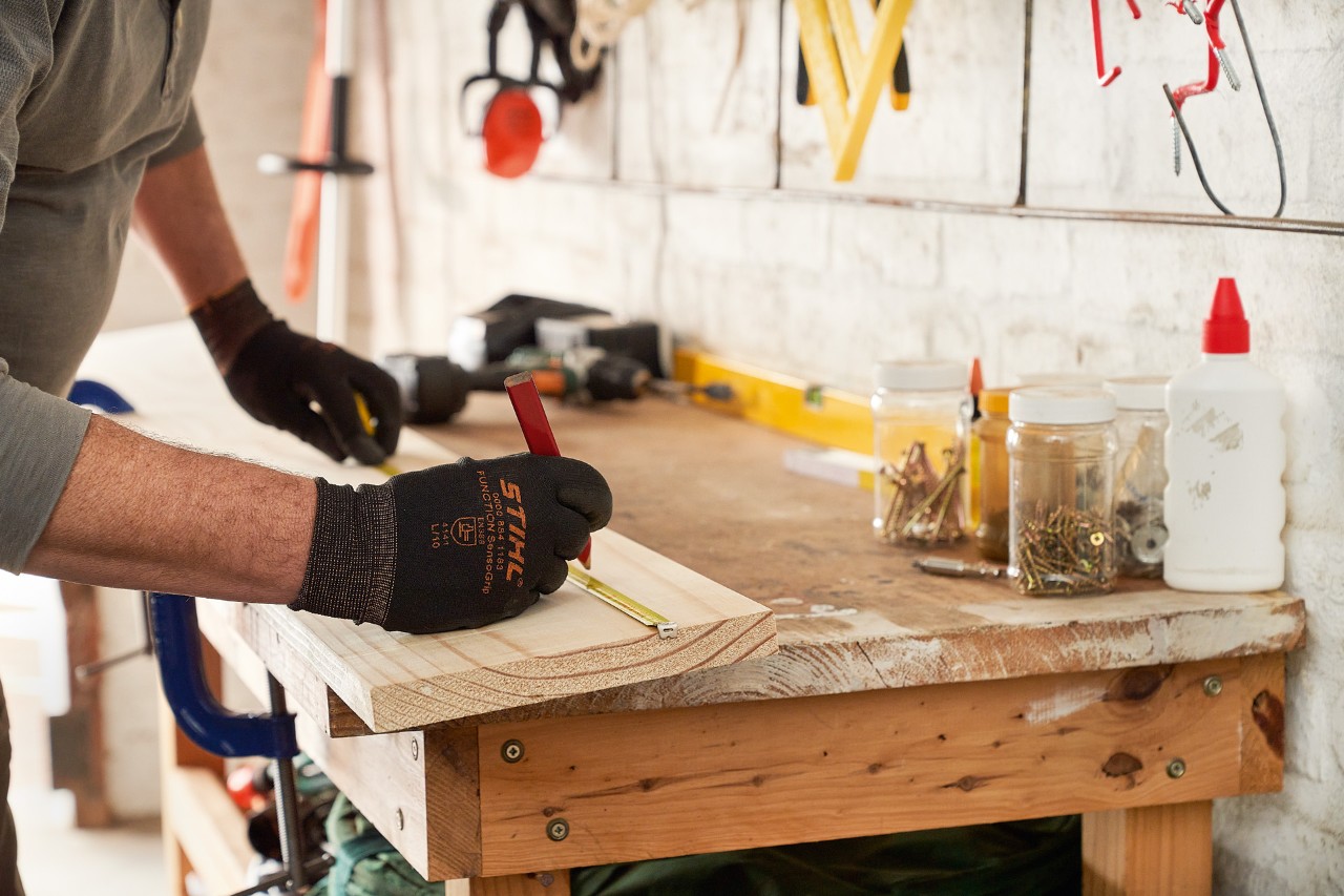 Man met STIHL veiligheidshandschoenen markeert boorgaten op een houten plank