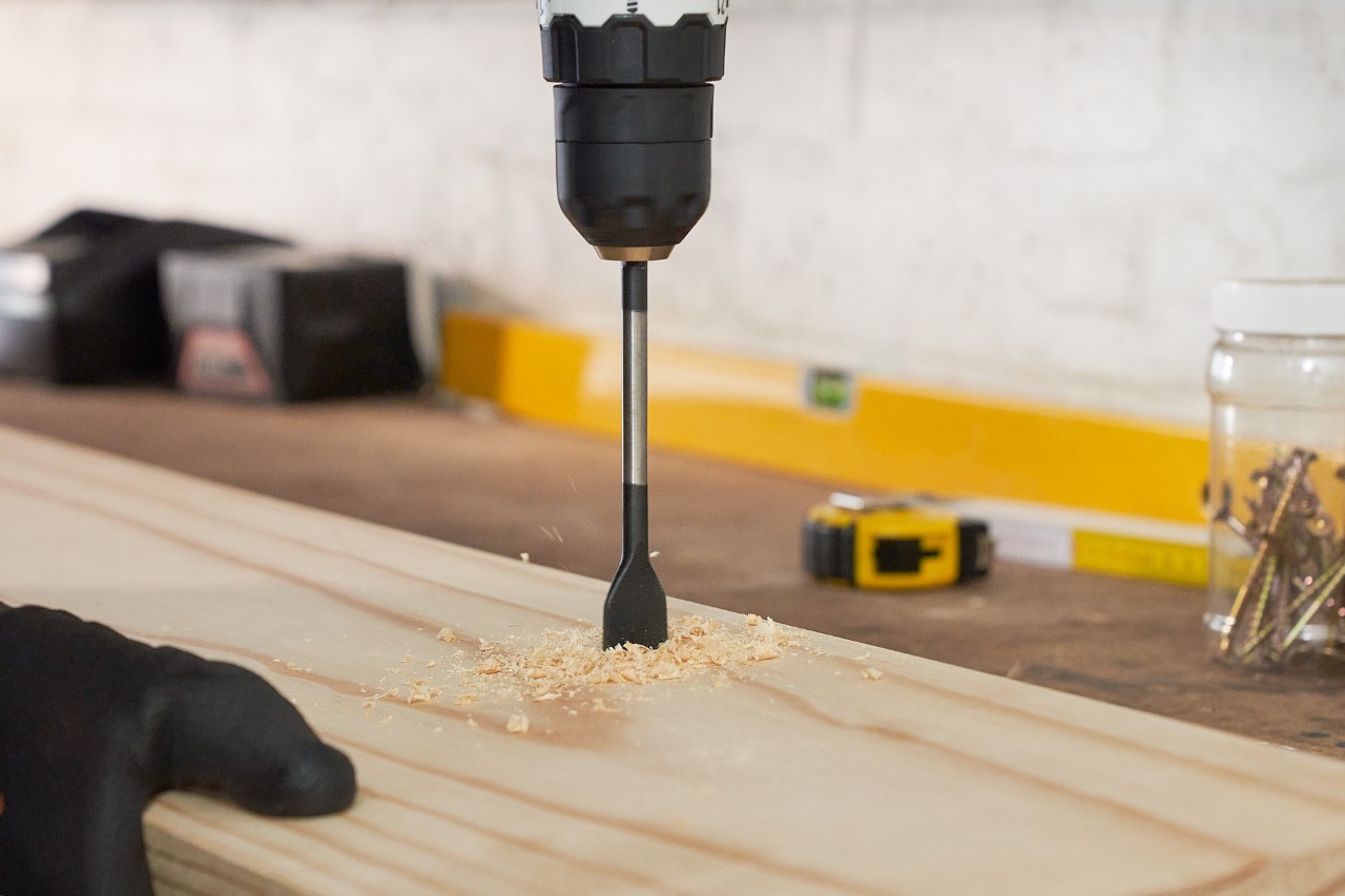 Iemand boort gaten in een houten plank om een eigen tuingereedschaphouder te maken