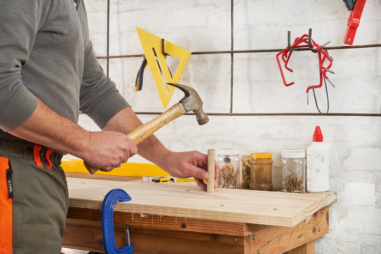 Een man slaat met de hamer een stokje in het boorgat van een houten plank