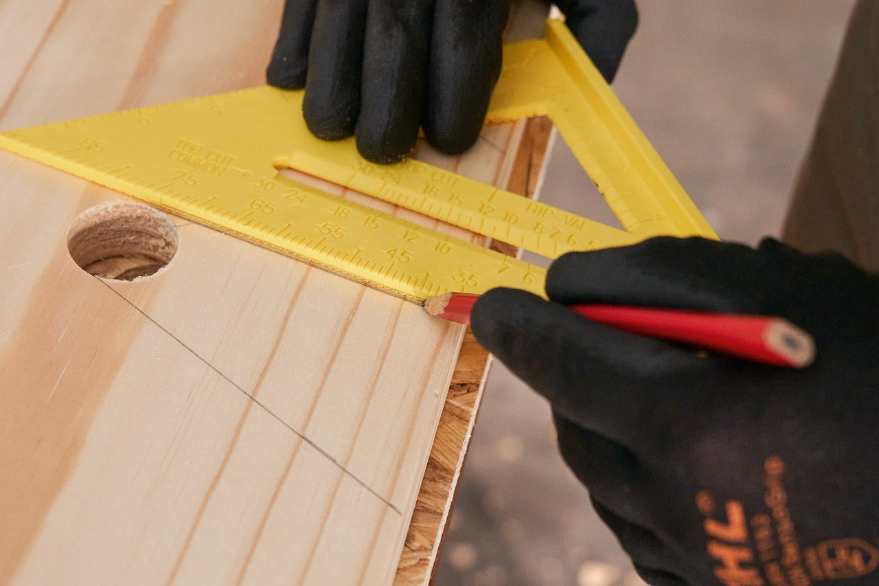 Iemand tekent met potlood en geodriehoek lijnen op een houten plank om uitsparingen te markeren 