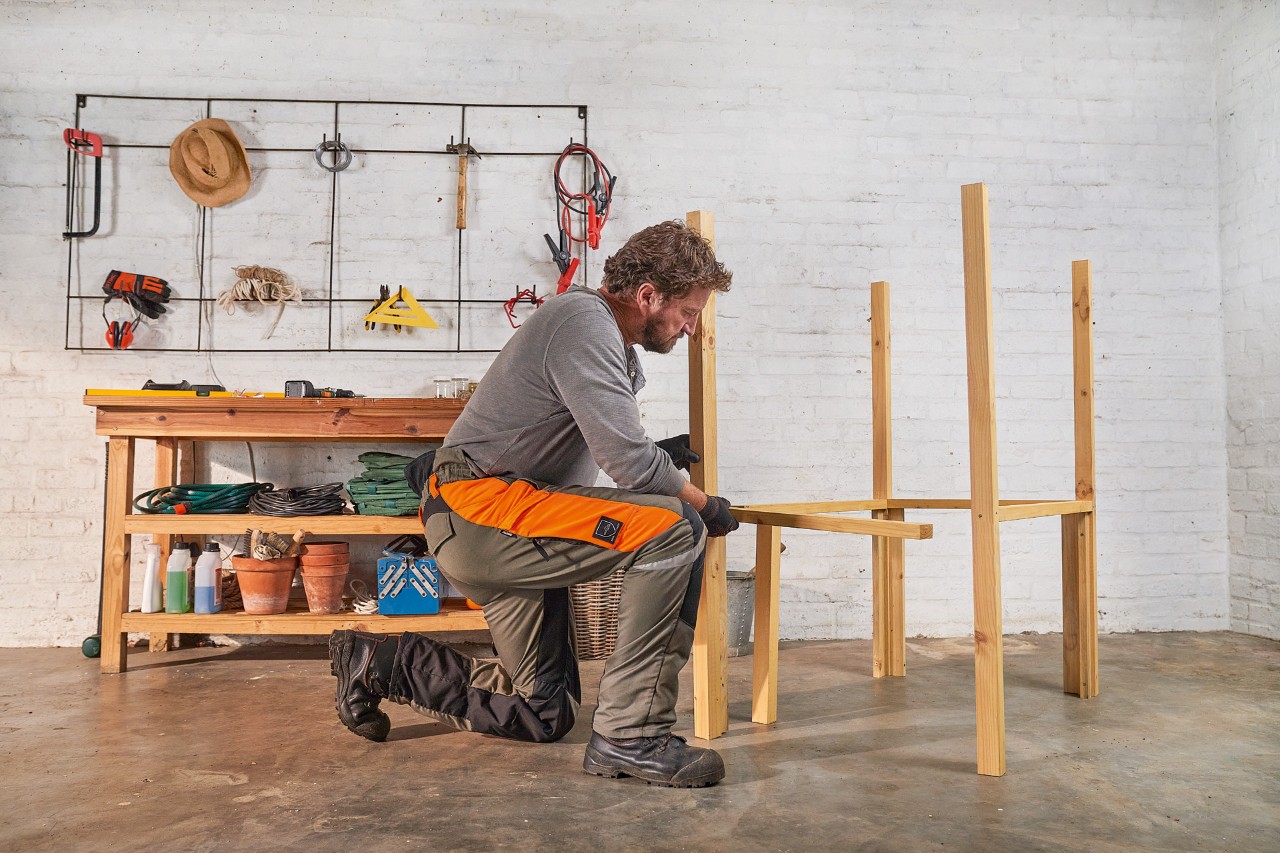 Een man schroeft dwarsbalken aan staanders vast om een eigen berging voor de grasmaaier te maken