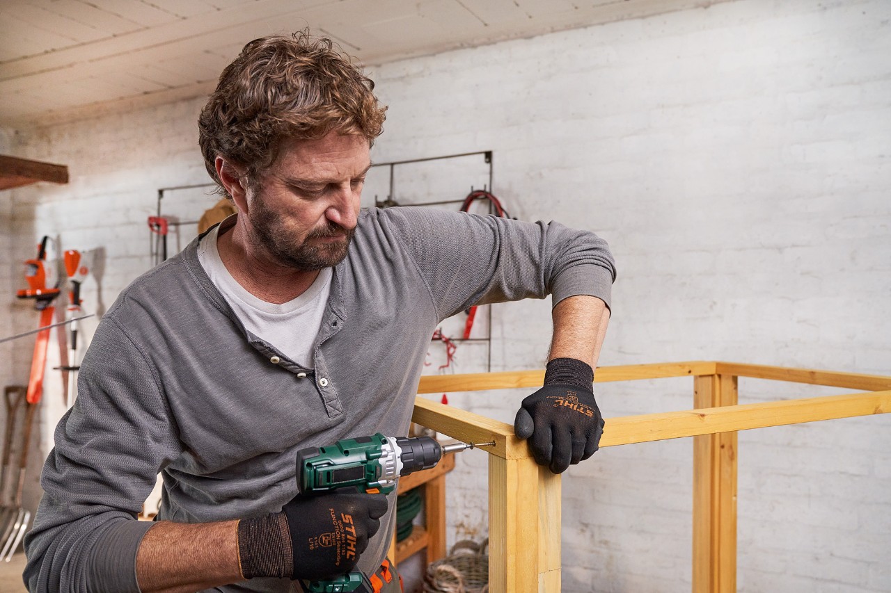 Een man maakt uit balken een dakframe voor de berging voor de grasmaaier
