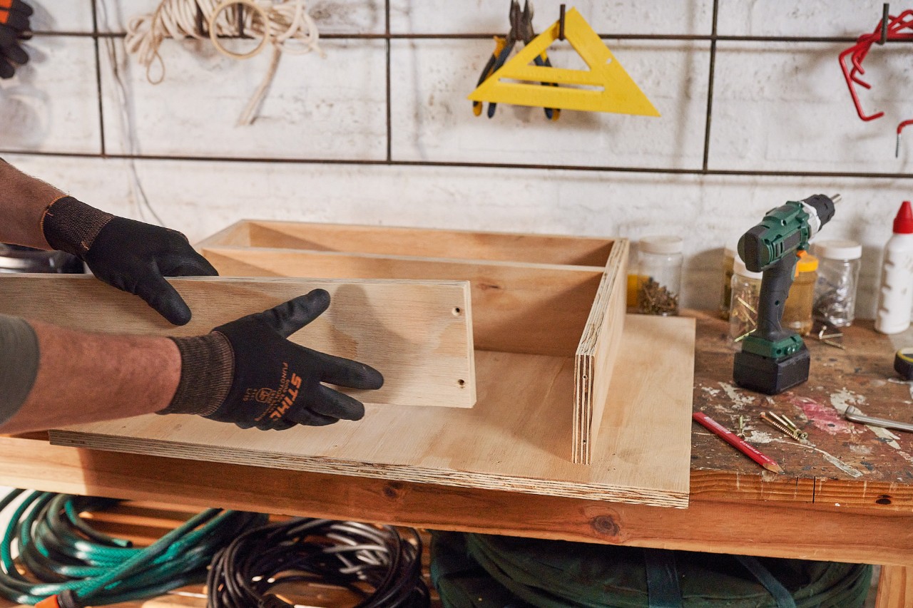 Man bouwt lade van houten planken voor de berging voor de grasmaaier 