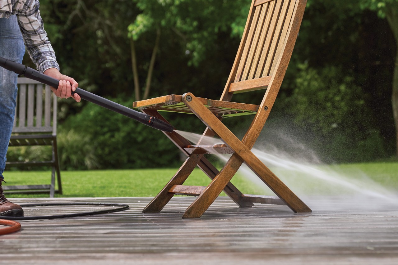 Een houten tuinstoel op een terras wordt schoongemaakt met een waterstraal van een STIHL RE 130 Plus hogedrukreiniger