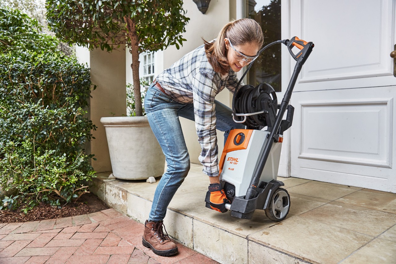 Een vrouw die een STIHL RE 130 Plus hogedrukreiniger een trapje aftilt naar een stenen pad