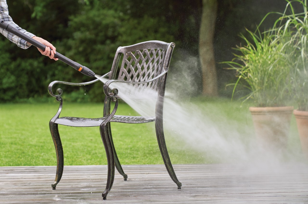 Een metalen tuinstoel die wordt gereinigd met een waterstraal van de STIHL RE 130 Plus hogedrukreiniger