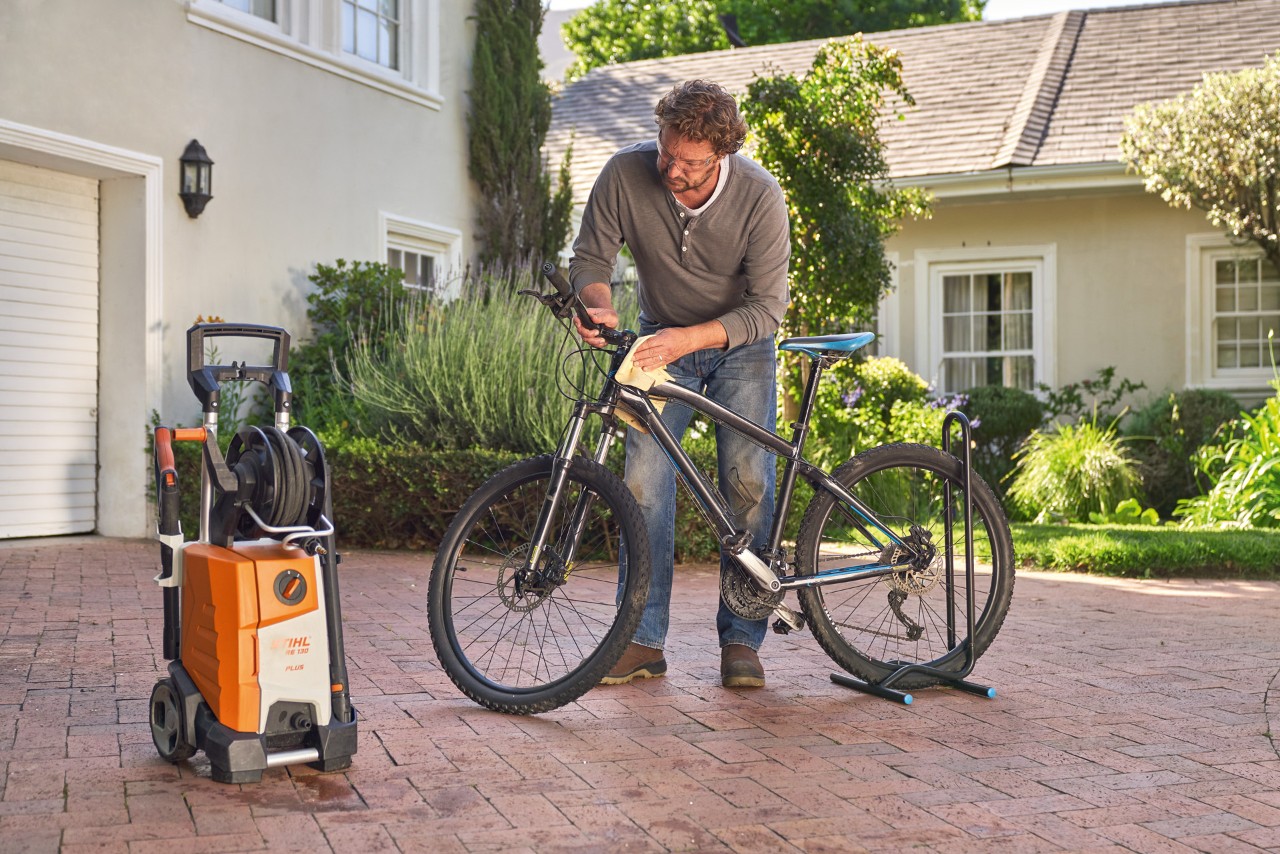 Een man droogt een fiets met een doek, met een STIHL RE 130 Plus hogedrukreiniger ernaast