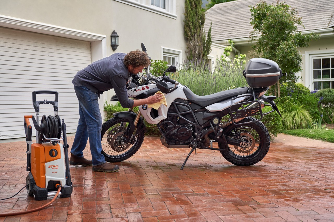 Een man droogt een motor met een zeem, met een STIHL RE 130 Plus hogedrukreiniger ernaast