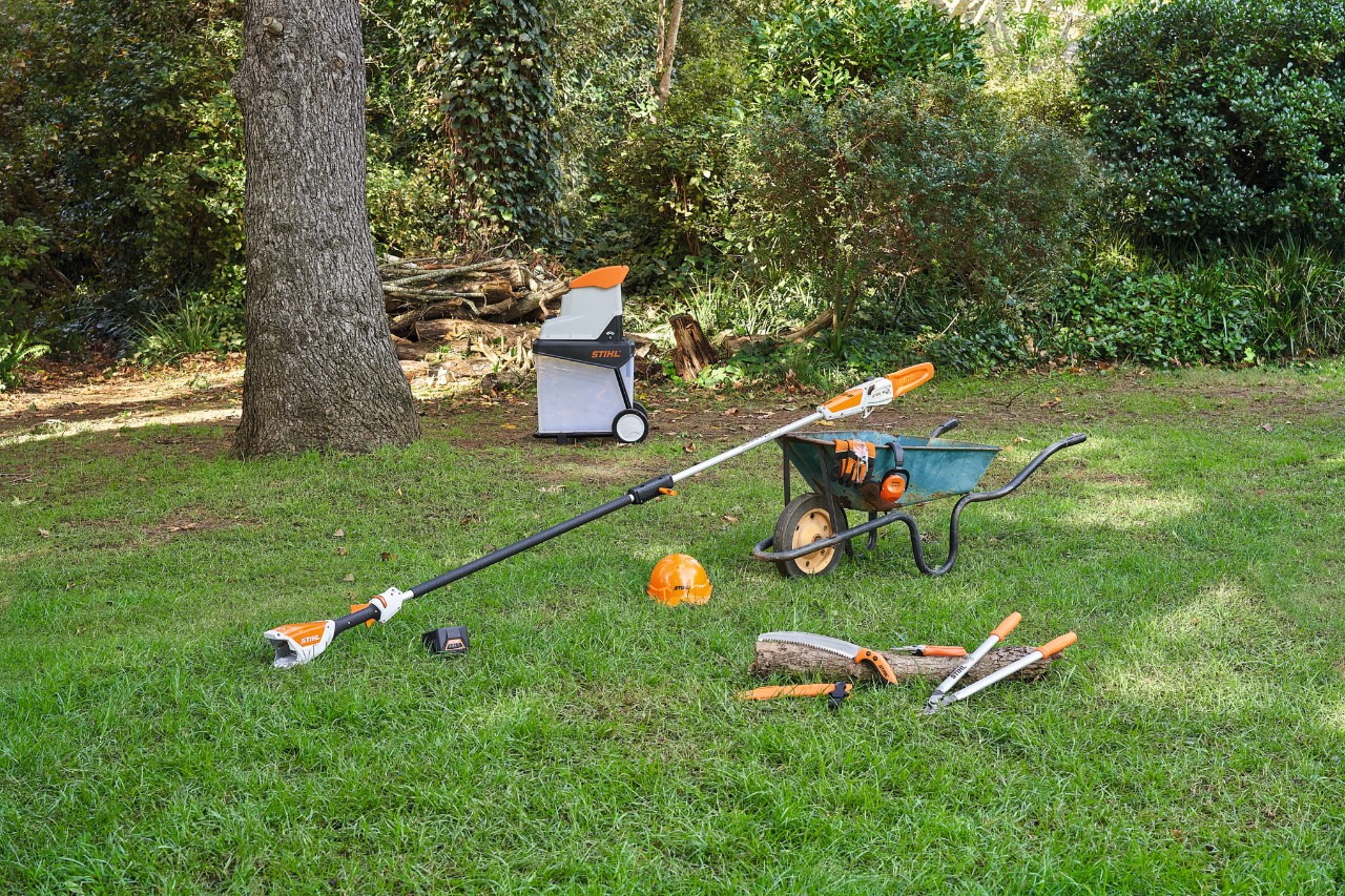 Verschillende apparaten, zoals een STIHL snoei- en takkenschaar, liggen op een gazon in een tuin om een appelboom te snoeien