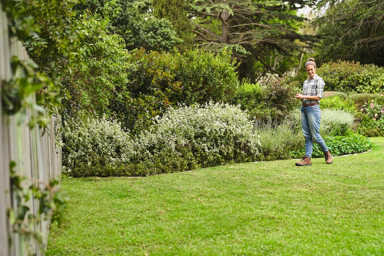 Vrouw loopt op haar pas gelegde grasmat in een grote tuin