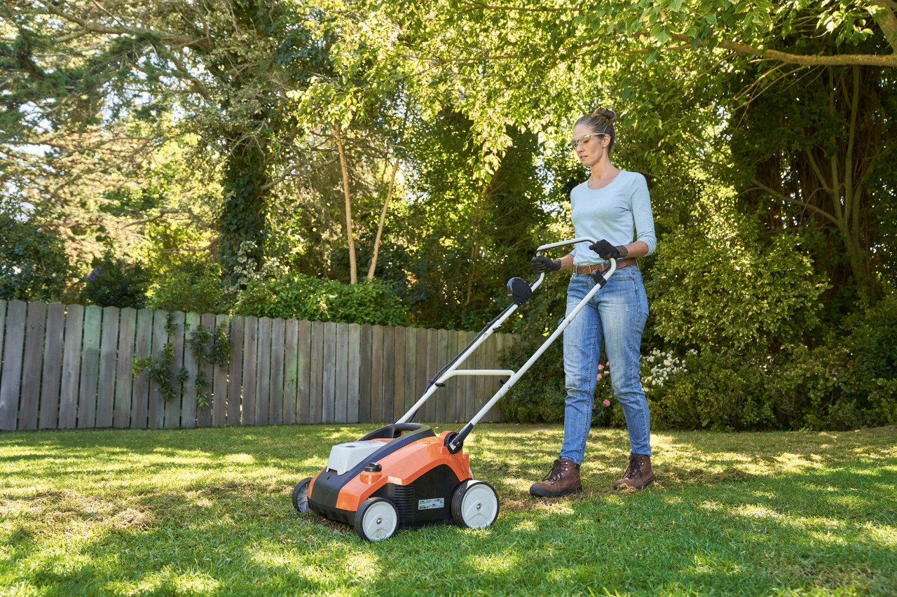 Vrouw met veiligheidsbril en werkhandschoenen verticuteert het gazon met de STIHL RLA 240 accuverticuteermachine