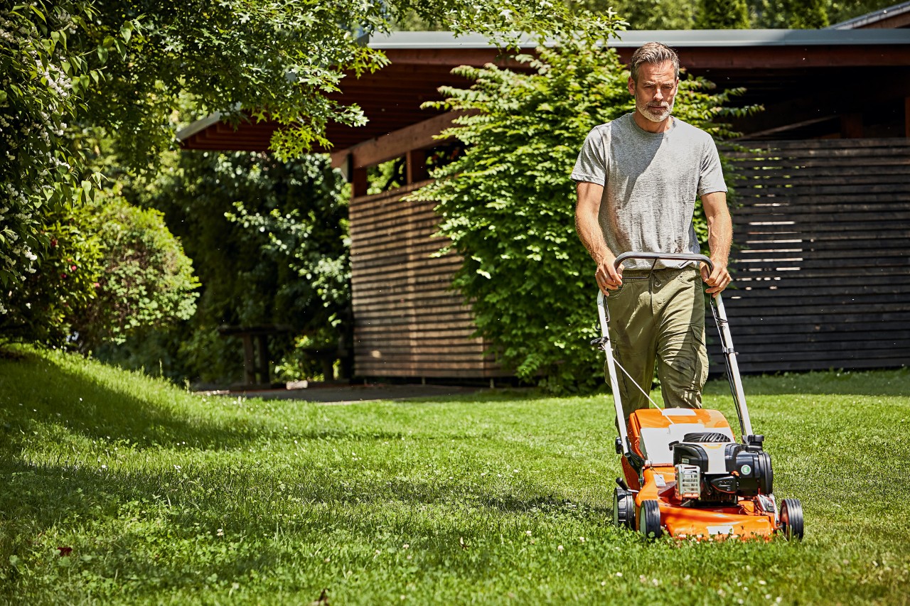  Man bij het grasmaaien met een STIHL RM 248 benzinegrasmaaier voor een tuinhuisje