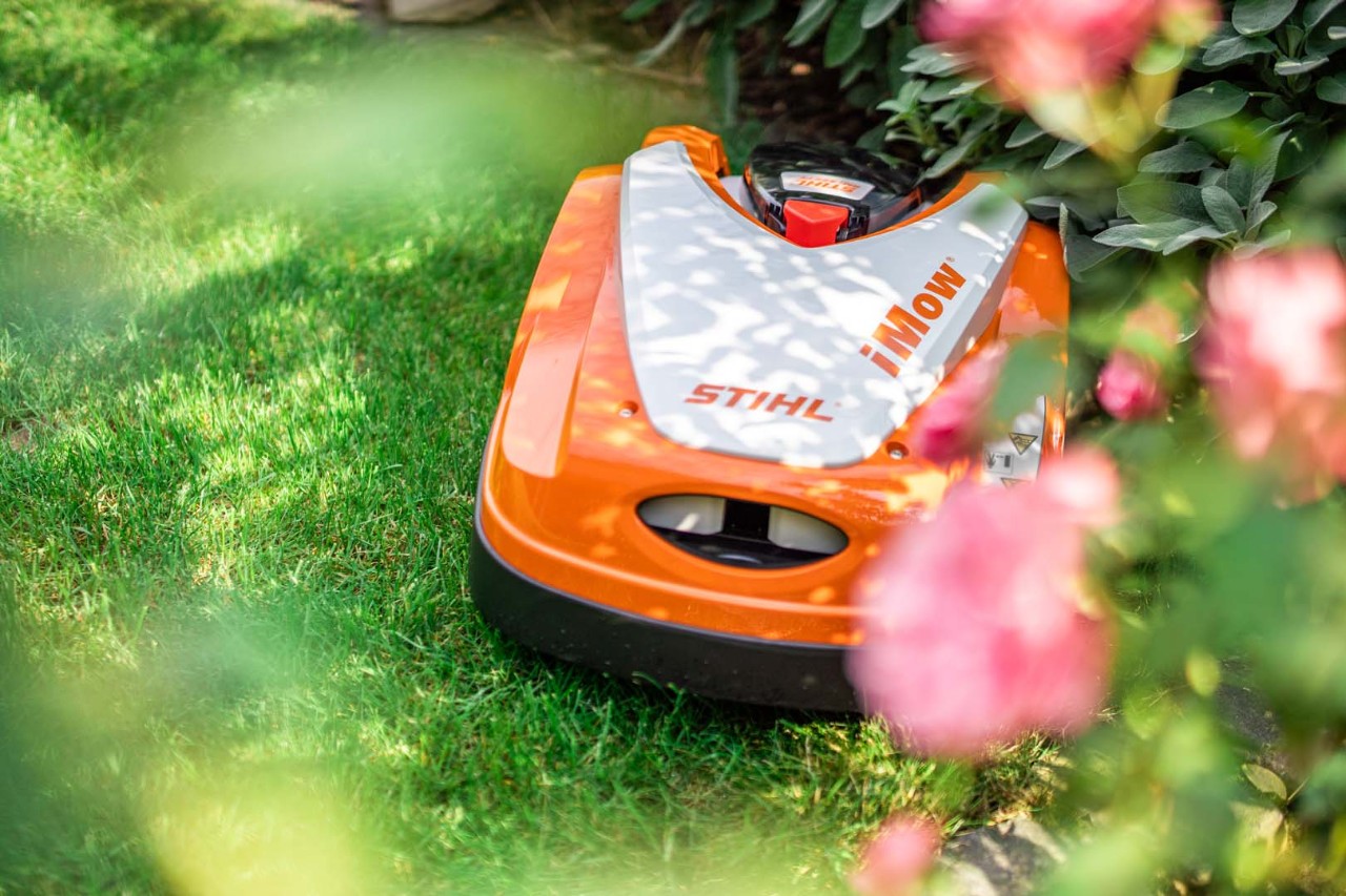 STIHL  RMI 422 P robotmaaier iMOW® op groen gazon achter een bloeiende struik