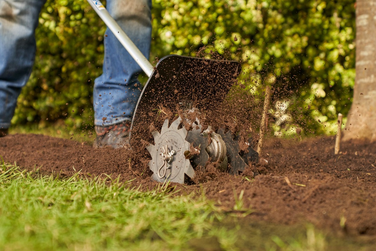 Een persoon maakt met een STIHL tuinfrees de grond in de tuin los om later een gazon aan te leggen