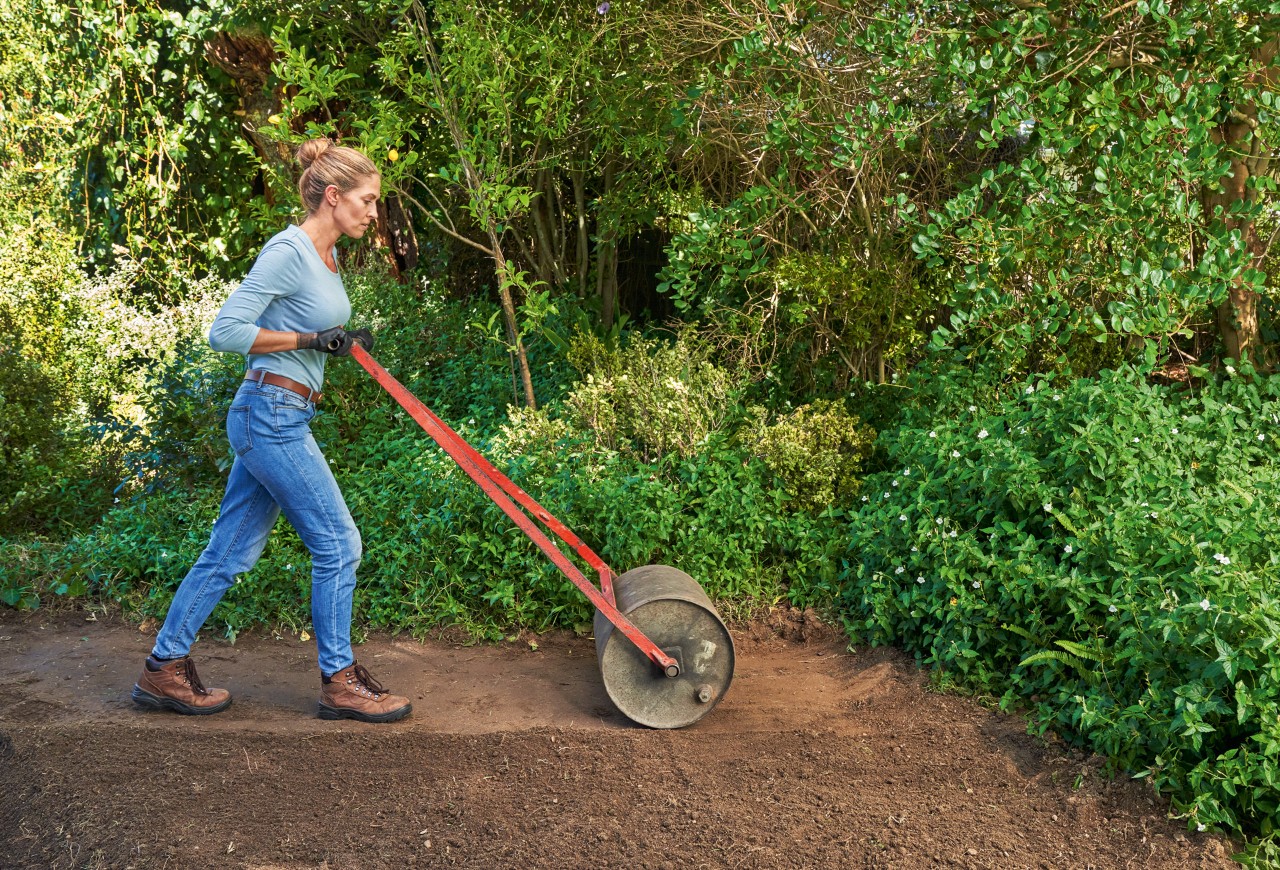 Vrouw comprimeert grond met een wals om een gazon aan te leggen