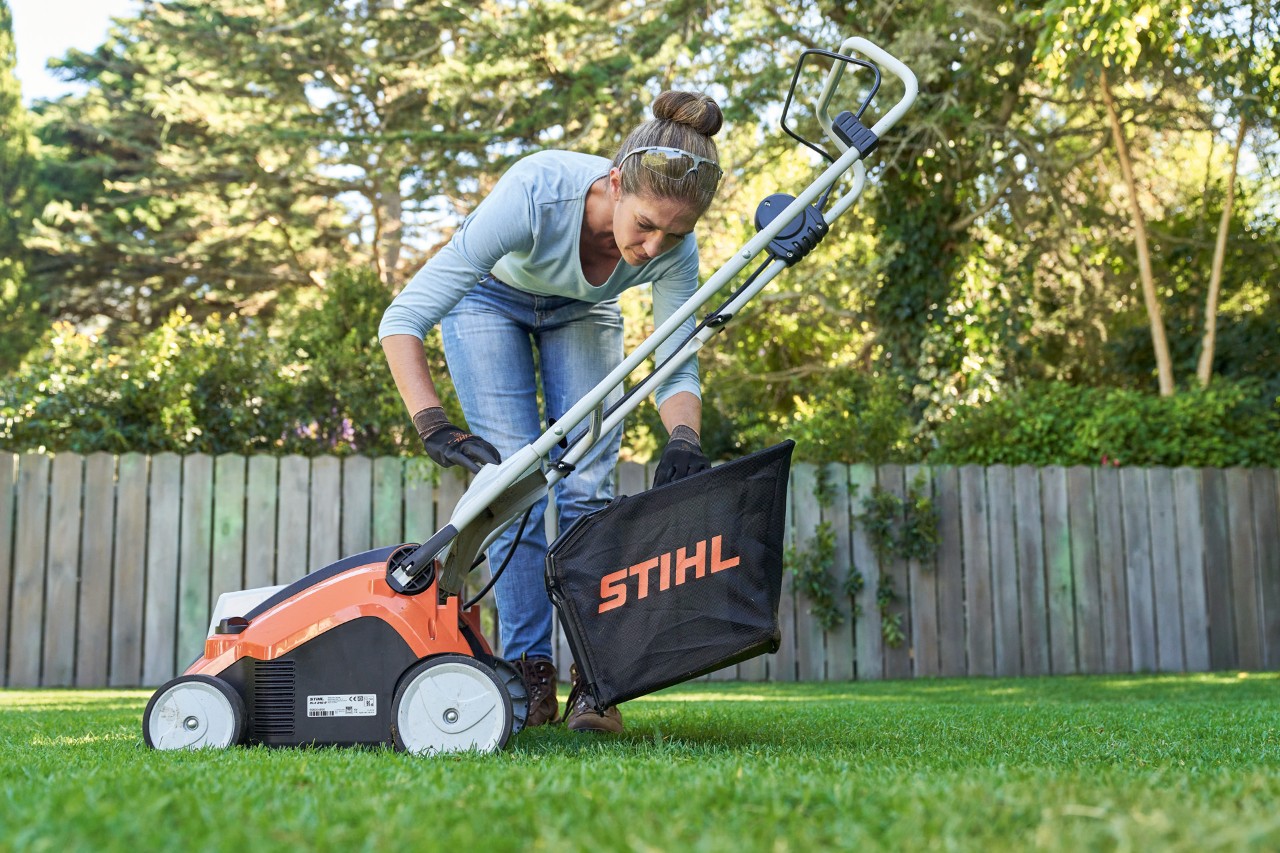 Vrouw bevestigt een opvangbak van de STIHL RLA 240 accuverticuteermachine achter aan de machine.