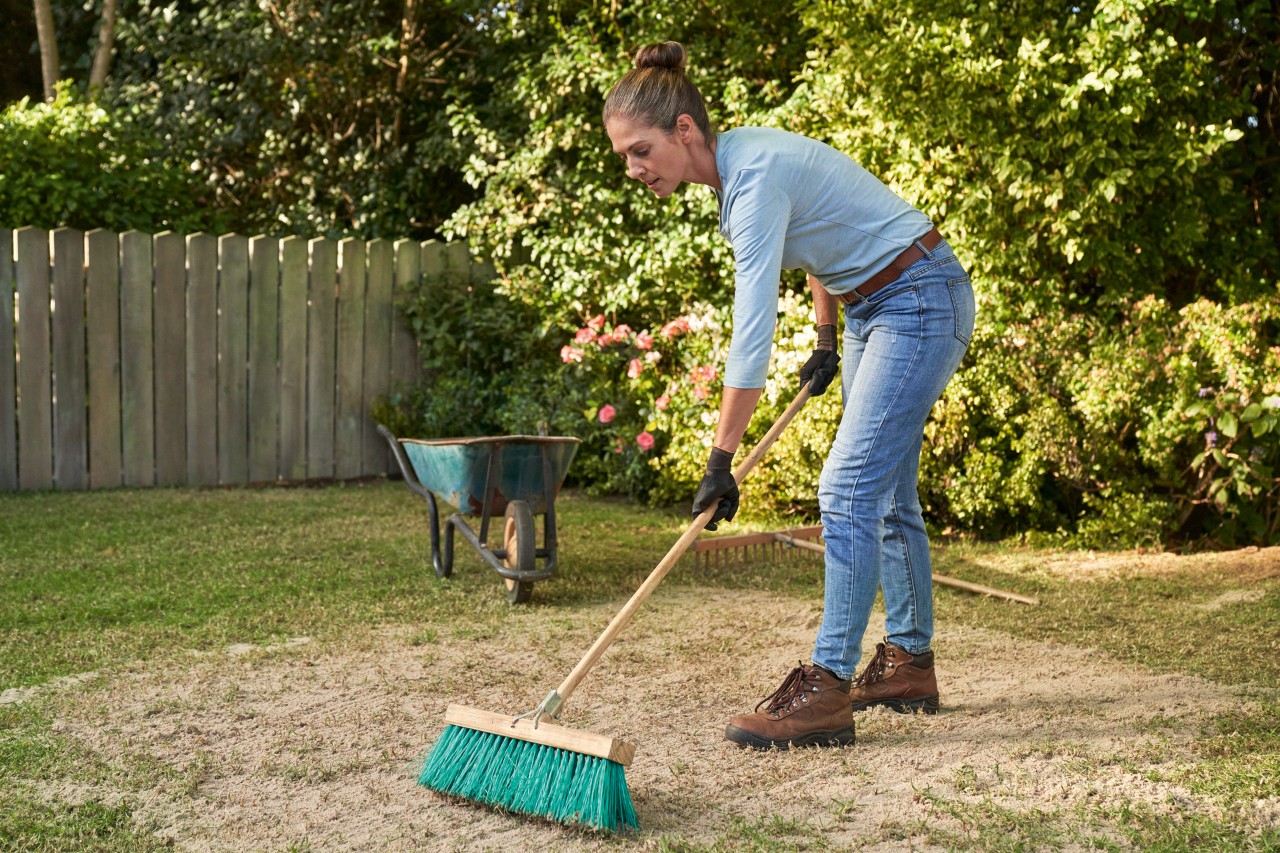 Een vrouw met een bezem in de hand is het gazon aan het bezanden