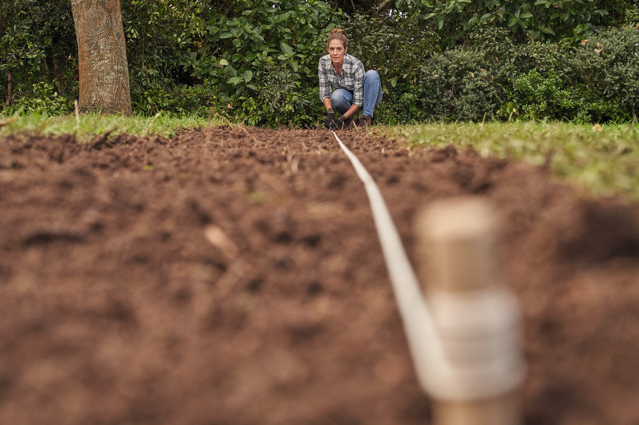 Vrouw verbindt twee houten stokjes met een touw om hoogteverschillen van een gazon te bepalen