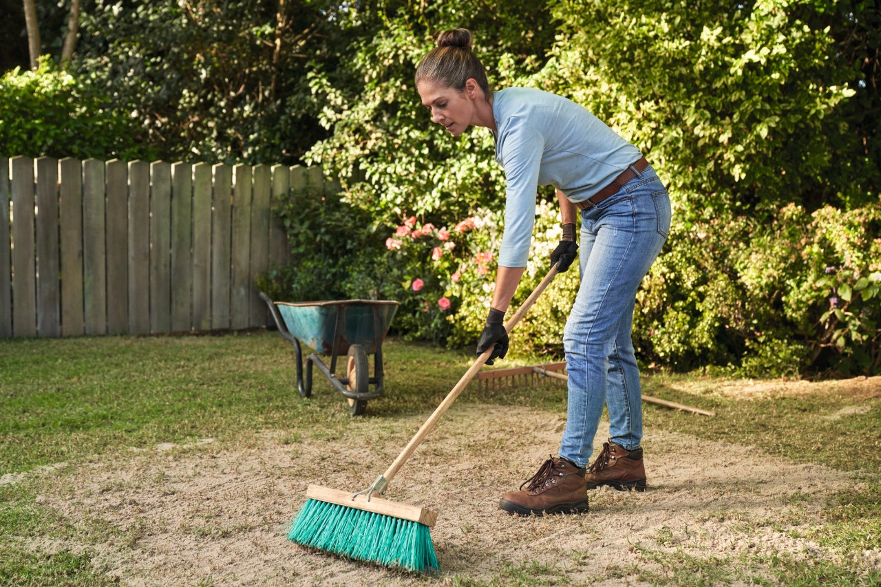 Een vrouw verdeelt met een bezem zand over het gazon om het te egaliseren