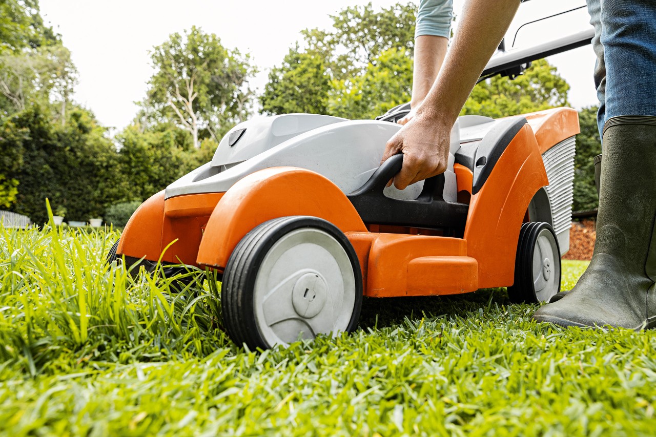Een STIHL RMA 339 C accugrasmaaier op een gedeeltelijk gemaaid gazon, met een persoon die de grasopvangbak verwijdert