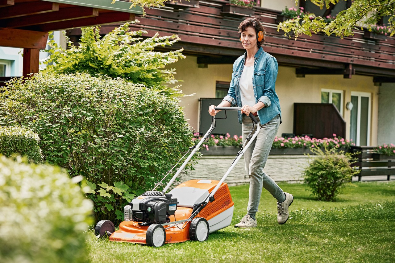 Een vrouw die een STIHL RM 243 T benzinegrasmaaier gebruikt in de tuin voor een huis