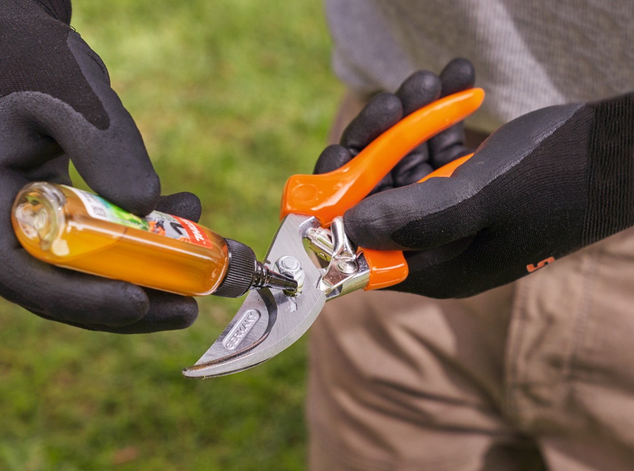 Iemand met STIHL werkhandschoenen smeert een snoeischaar