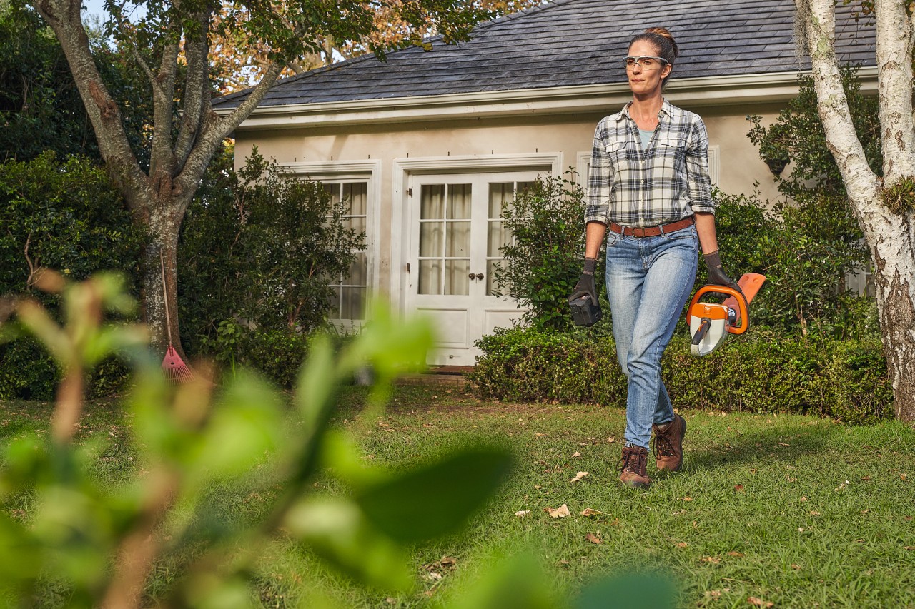 Vrouw loopt met een STIHL accuheggenschaar in de hand door een tuin