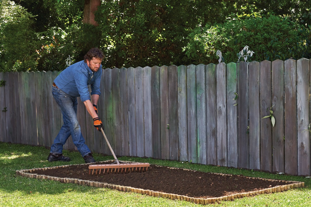 Persoon die grond egaliseert met een hark voor de aanleg van een plantenbed