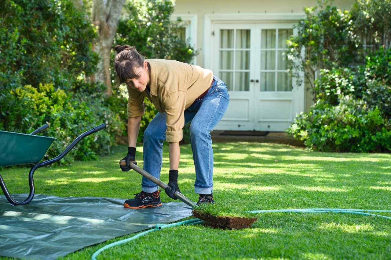Een vrouw verwijdert de grasnerf met een spade om een eilandperk aan te leggen
