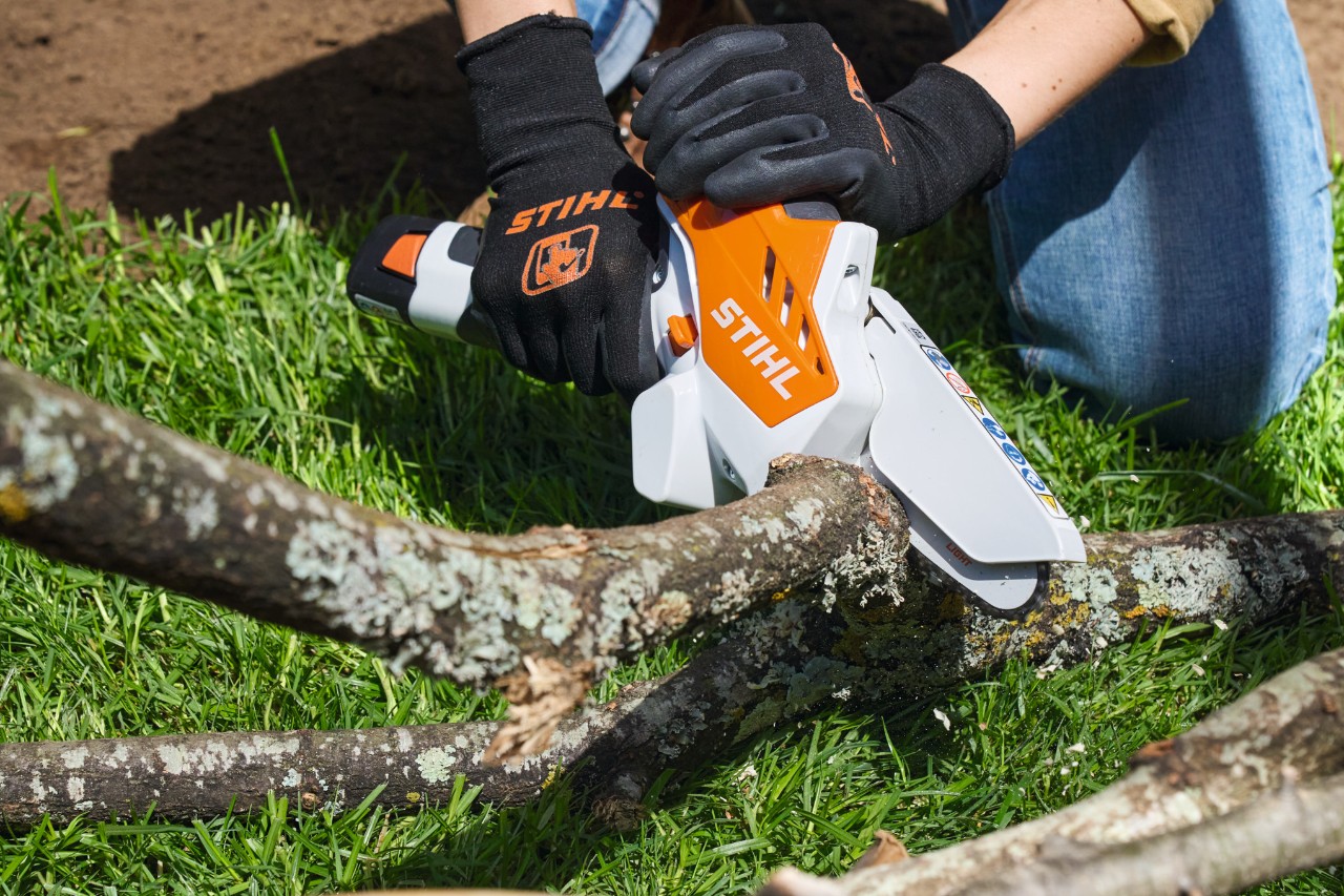Een persoon met veiligheidshandschoenen zaagt takken in stukken met een STIHL GTA 26 accusnoeizaag