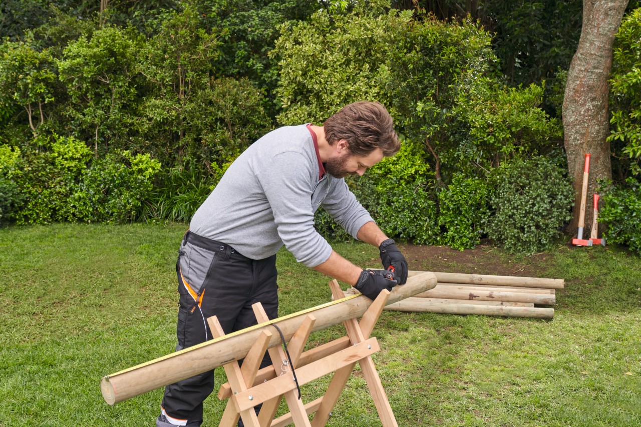 Een man meet takken op een houten bok en markeert de lengten