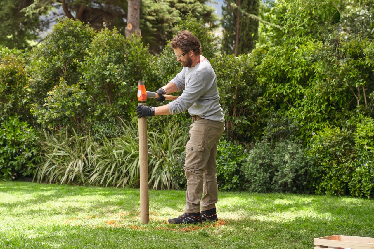Een man slaat met een hamer een houten paaltje in de grond
