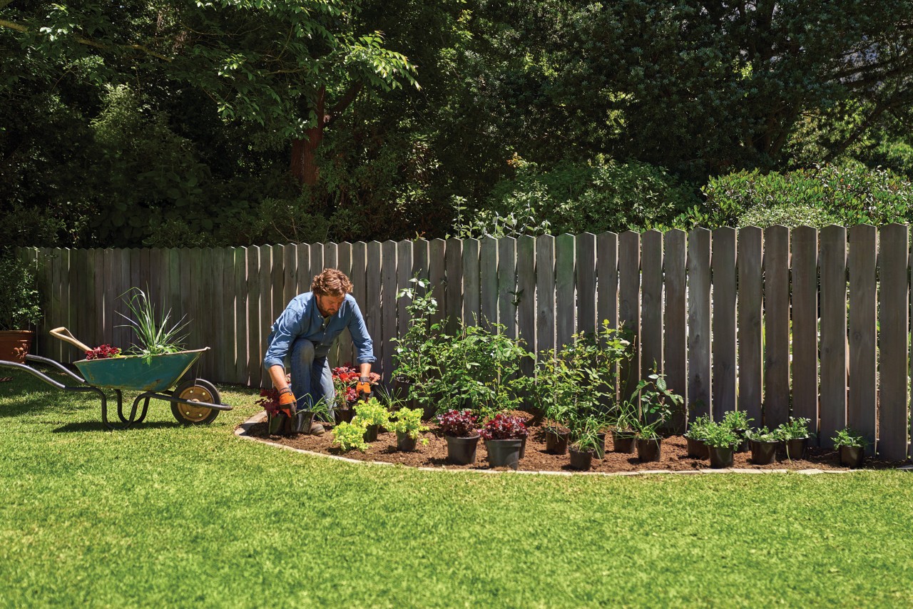 Een man die een tuinbed met potplanten beplant
