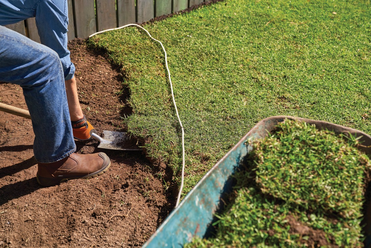 Man graaft zode uit de tuin met spade om een vaste plantenbed te maken