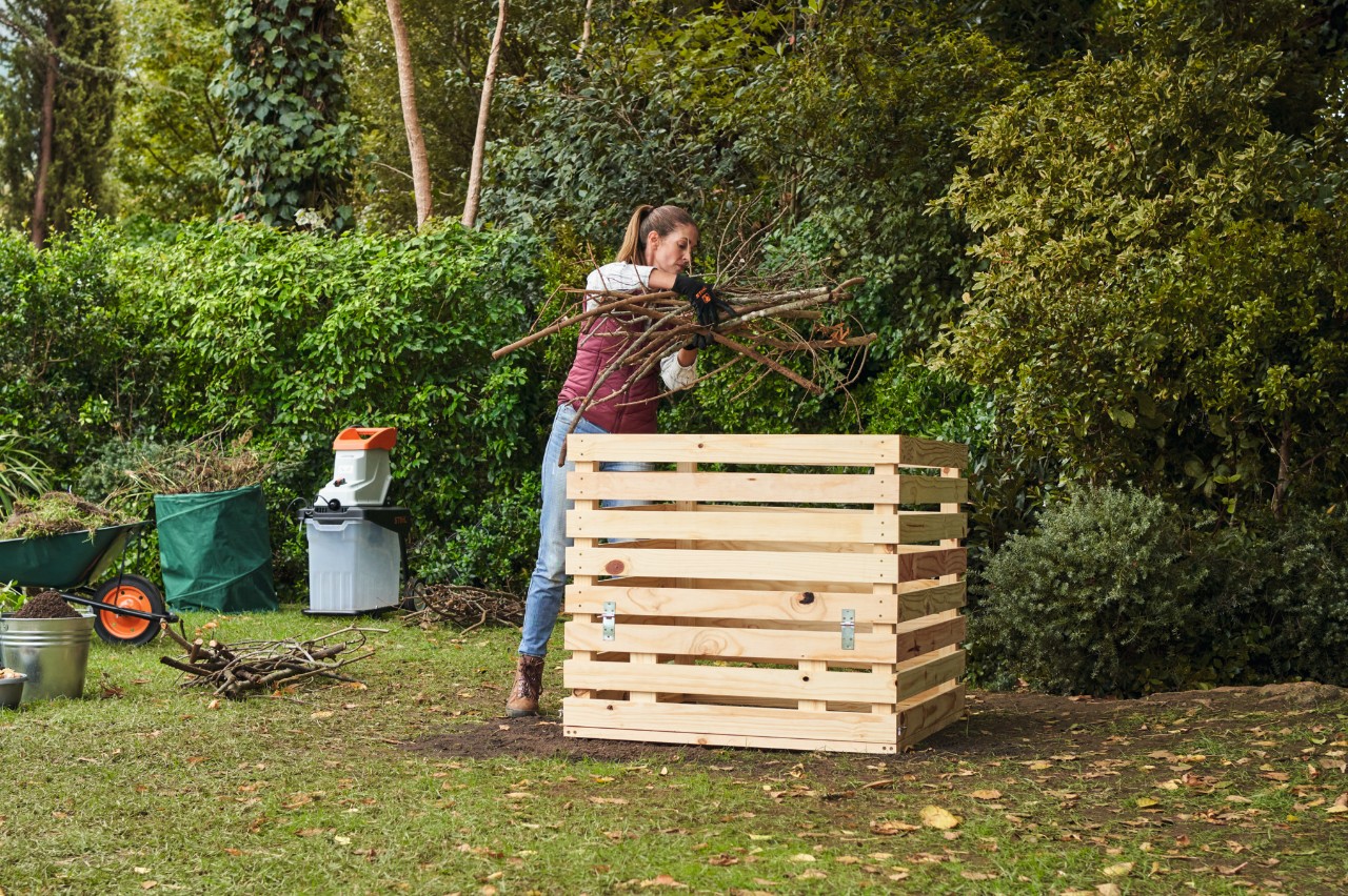 Een vrouw legt lagen droge takken in een houten compostbak