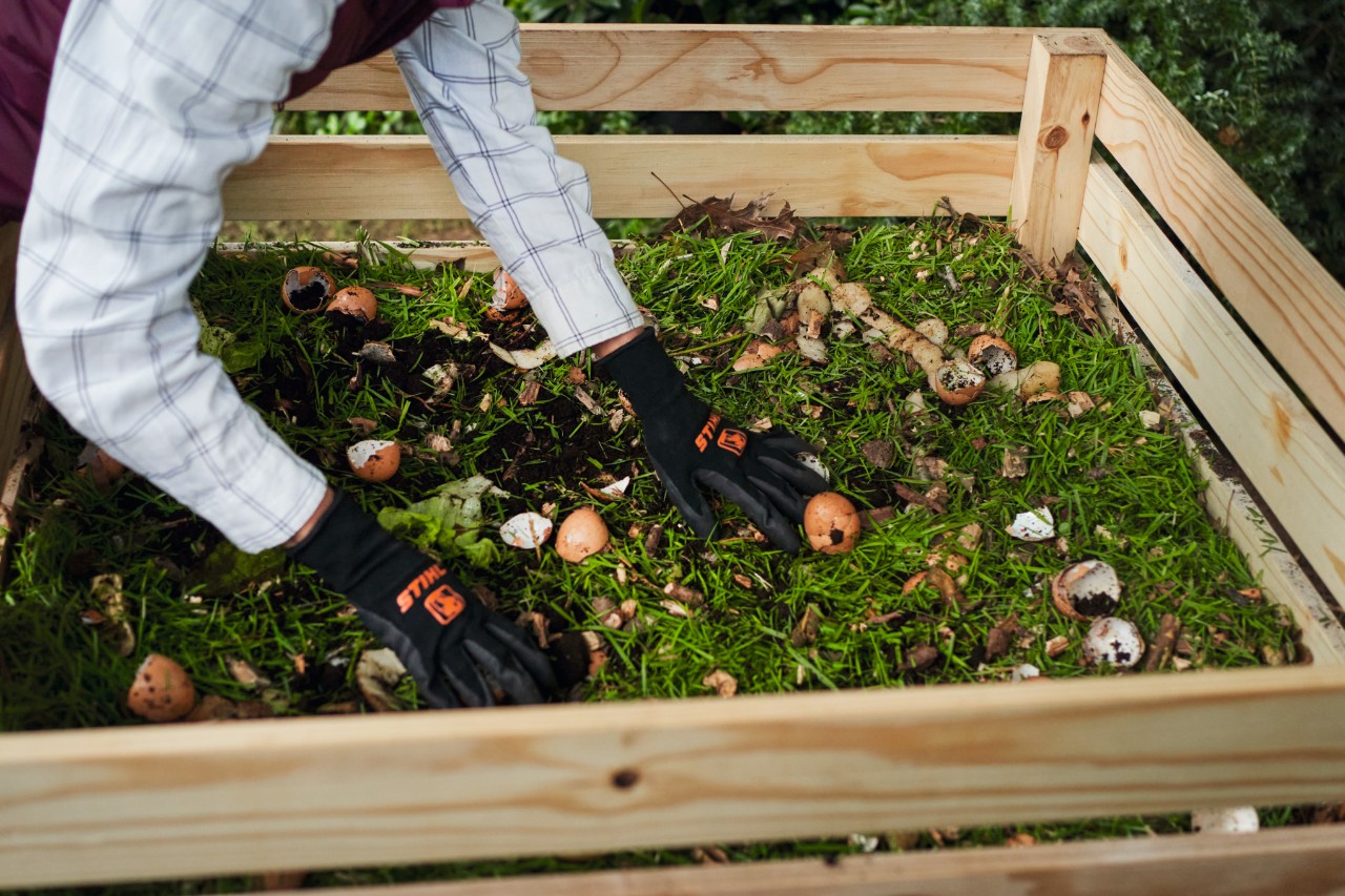 Close-up van een persoon die over een houten compostbak buigt en compost verdeelt