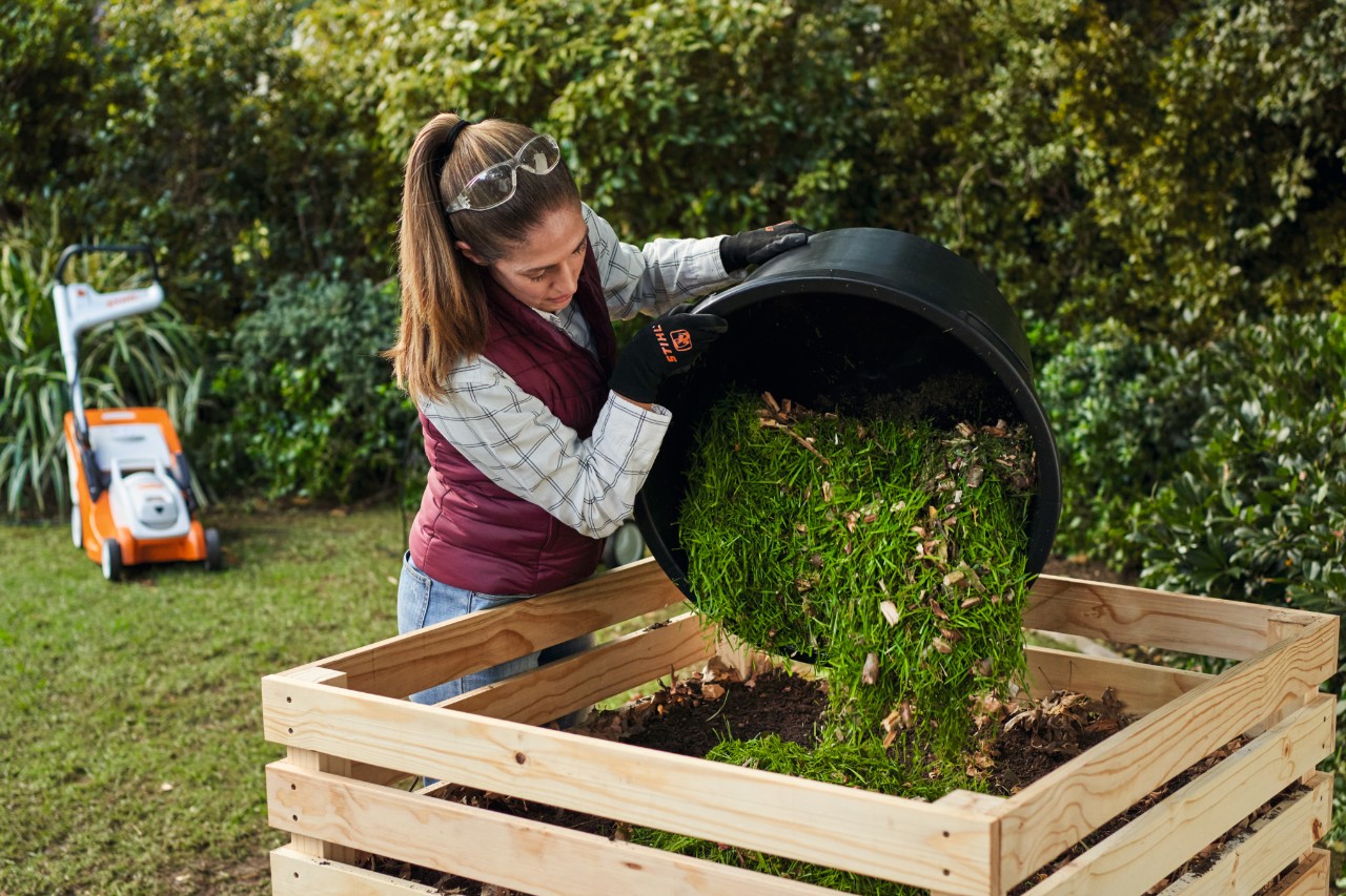 Vrouw stort emmer met groenafval in een compostbak