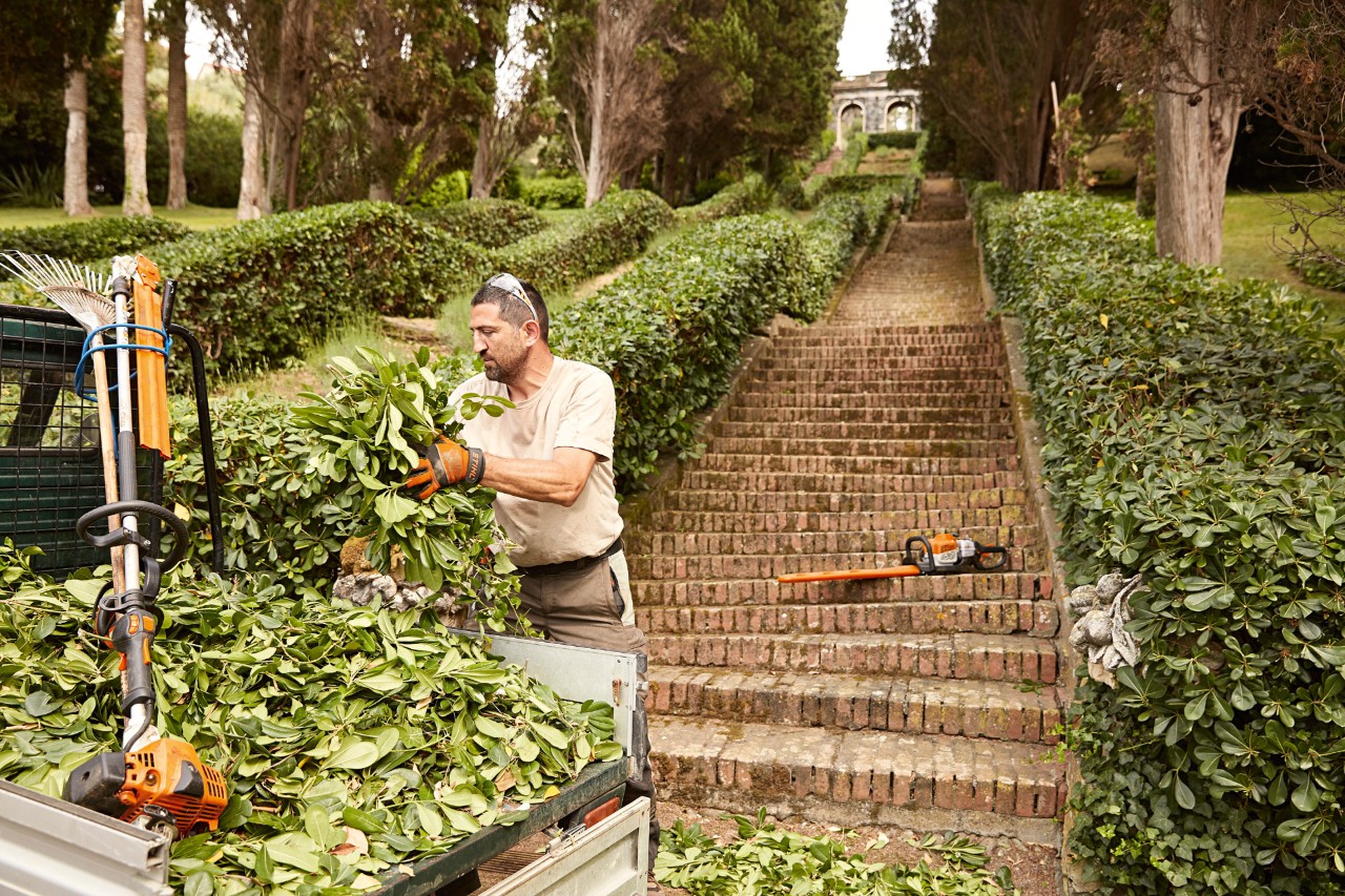 Tuinwerker vóór een trap met een haag laadt tuinafval op