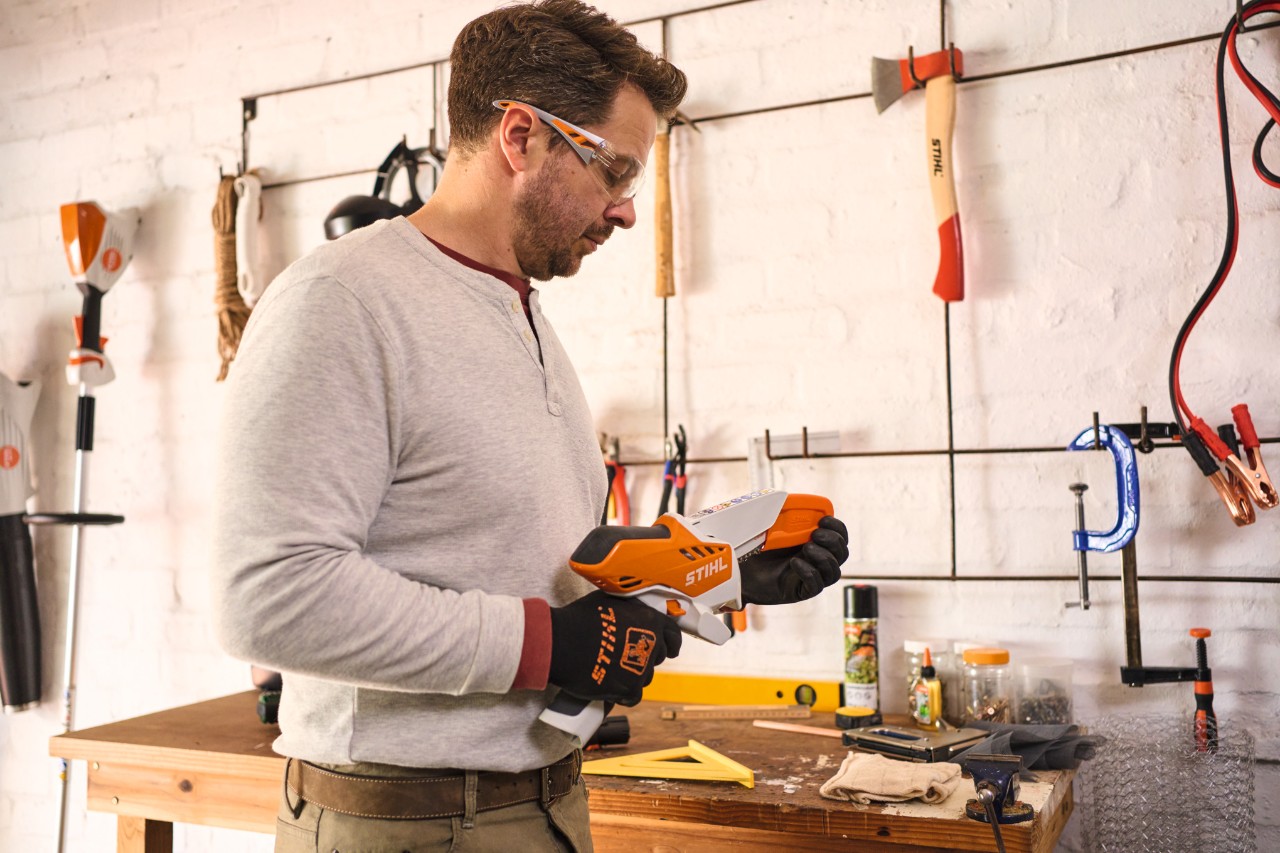 Een man met veiligheidsbril neemt de beschermkap van de STIHL GTA 26 accusnoeizaag weg