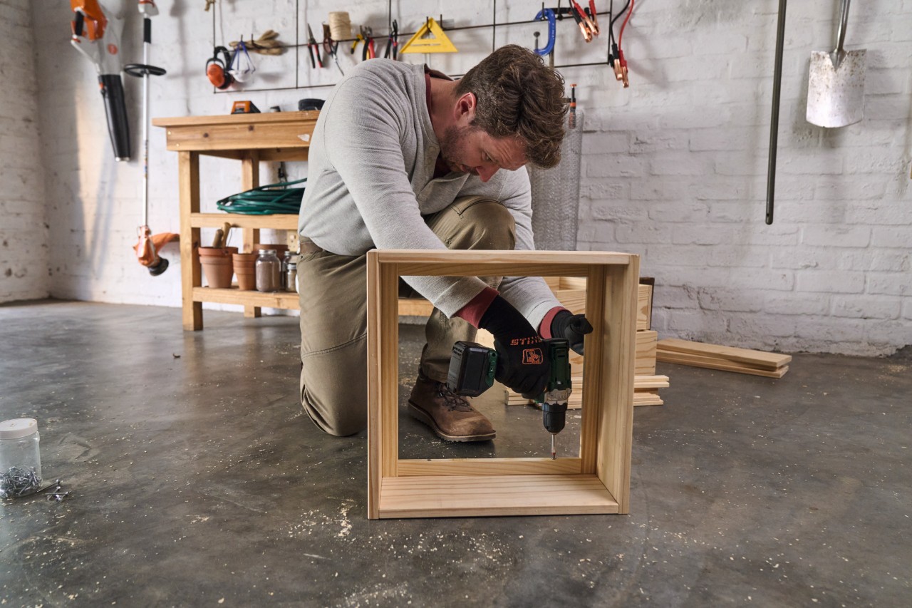 Een knielende man schroeft latten goed uitgelijnd op de kamer van de wormenkist