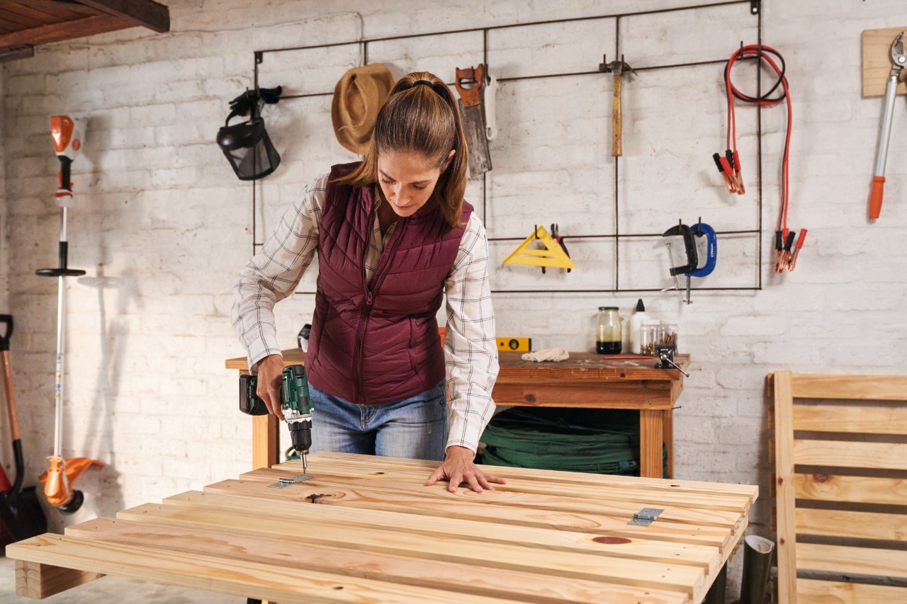 Vrouw schroeft op een werktafel een luik aan de voorkant van de compostbak vast met de accuschroevendraaier