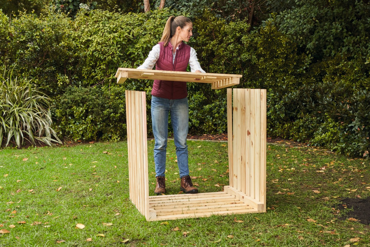 Vrouw in een tuin legt de voorkant voor de zelfgemaakte compostbak precies op de uitstekende zijwanden