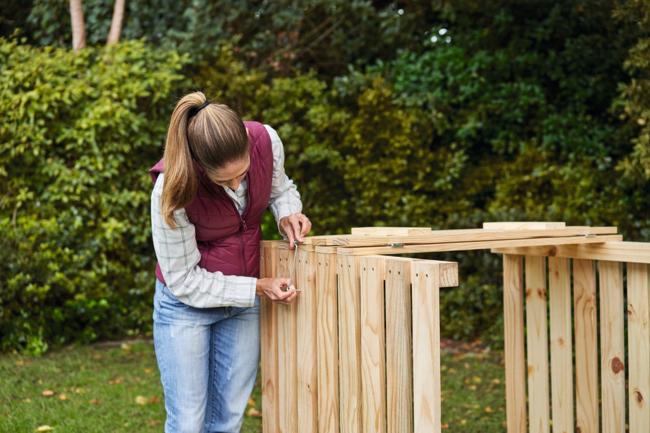 Vrouw in een tuin bevestigt windhaken aan een zelfgemaakte compostbak 
