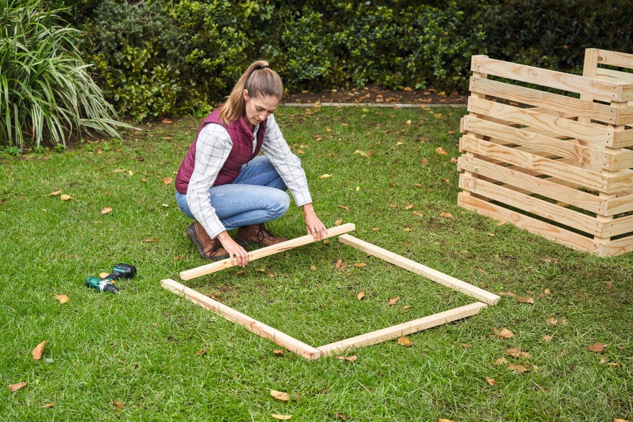 Vrouw bevestigt op een gazon latten in een rechte hoek voor het frame van de compostbak 