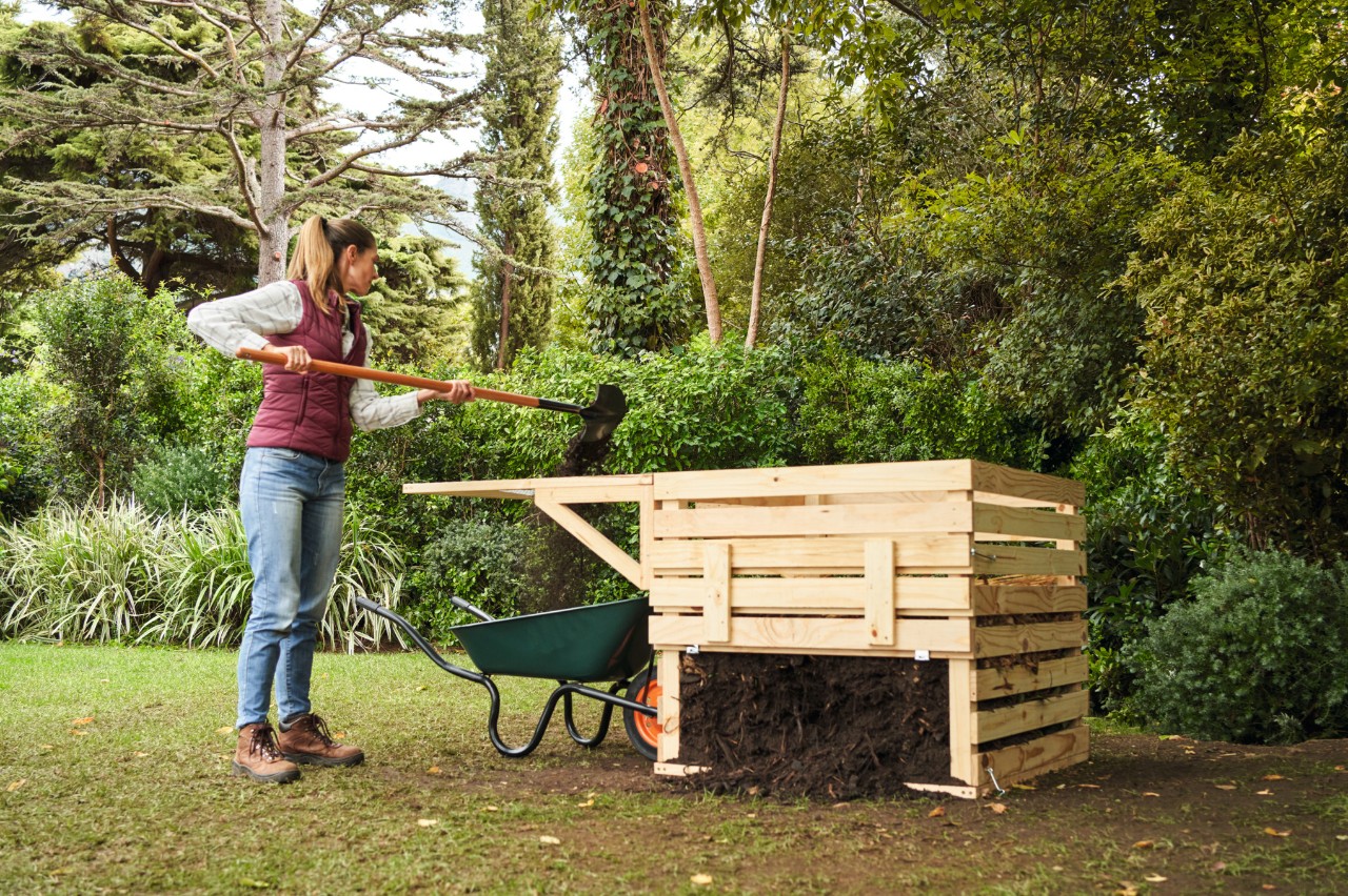 Vrouw zeeft ruw compost naast een zelfgemaakte houten compostbak in een tuin