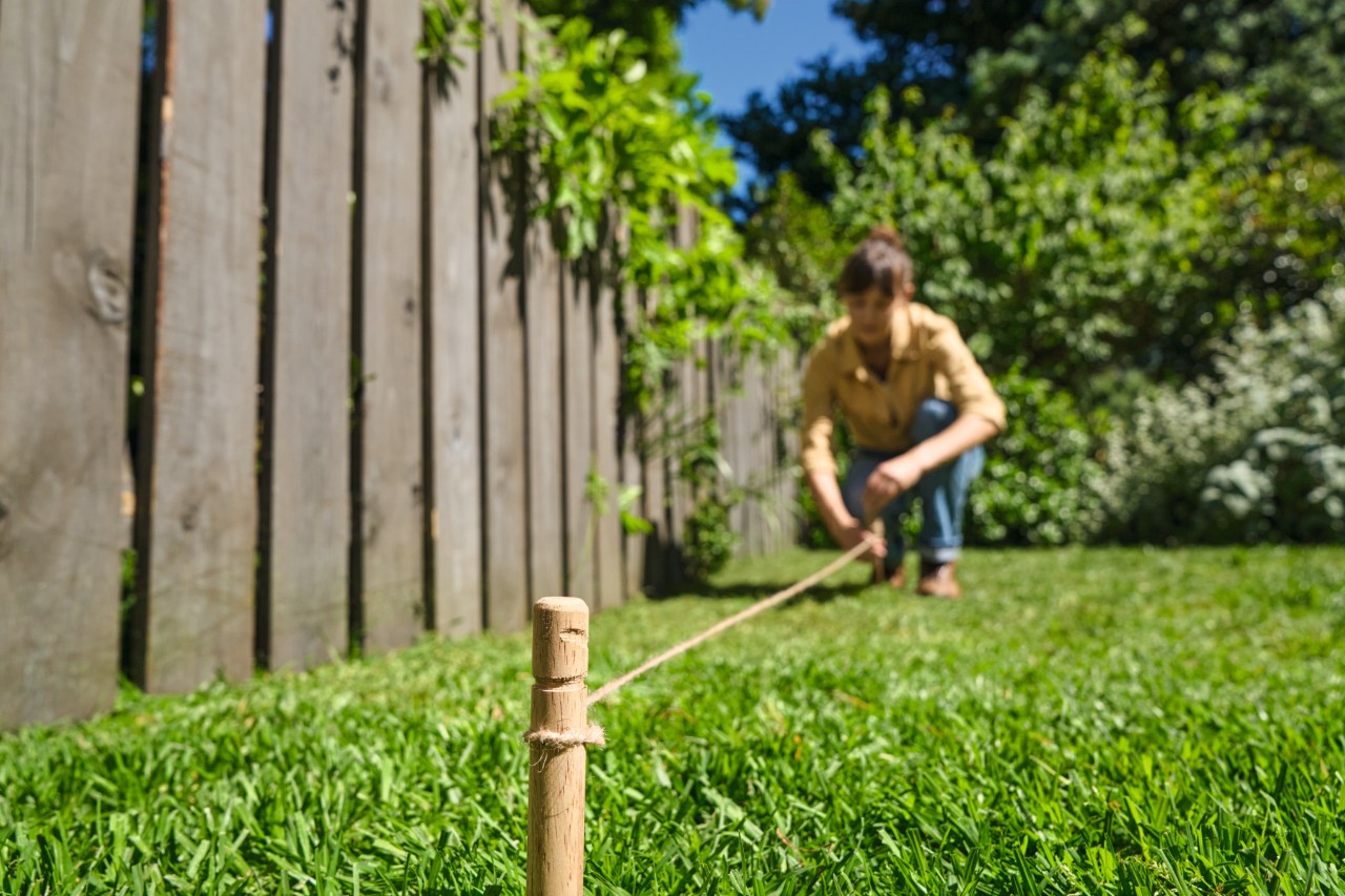 Een vrouw markeert de geplande rand van de bloemenstrook met houten paaltjes en een koord