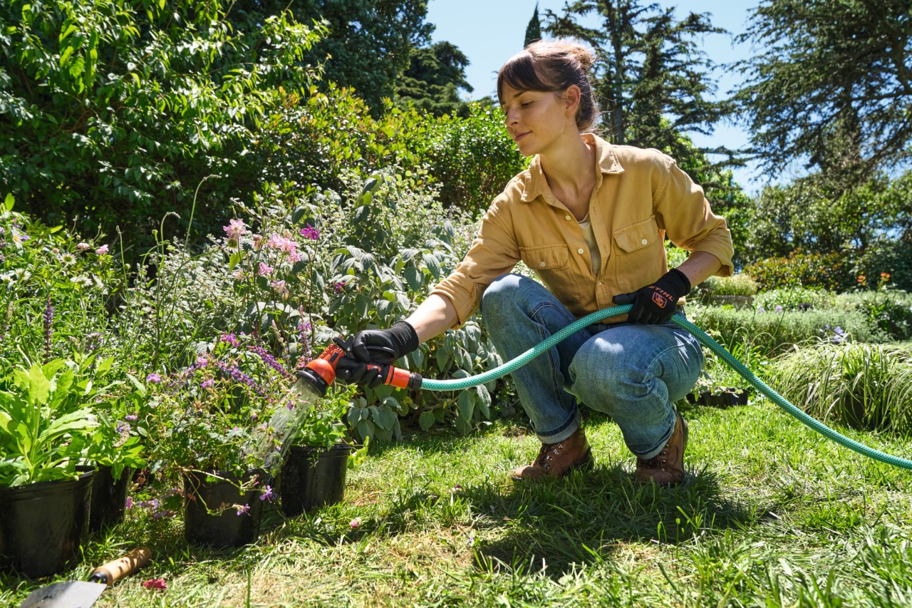 Een vrouw op een gazon geeft potplanten water met een tuinslang