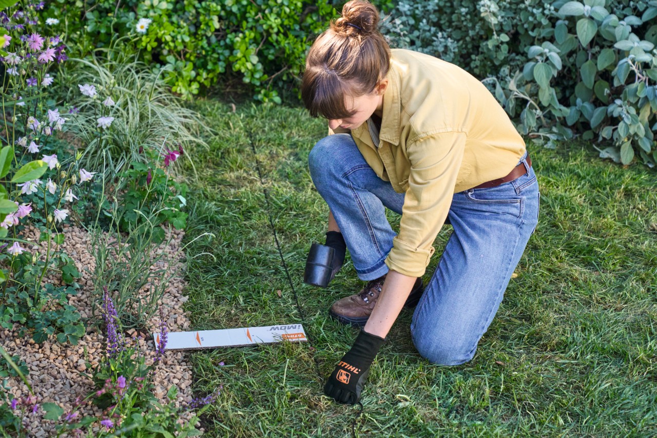 Een vrouw legt de begrenzingsdraad van de iMOW® op voldoende afstand van de bloemenstrook