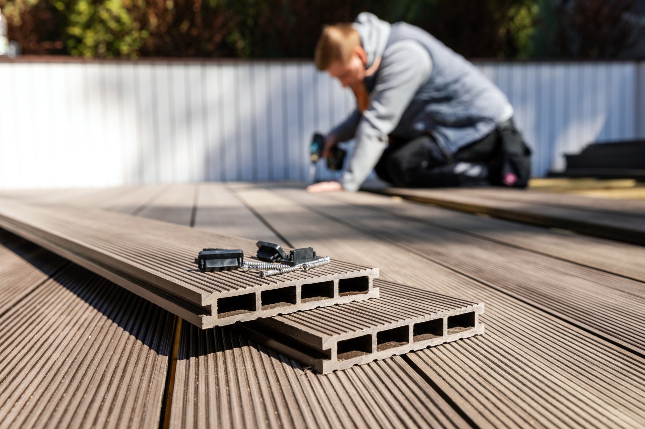 Man die WPC-vloer legt op een terras voor een witte omheining